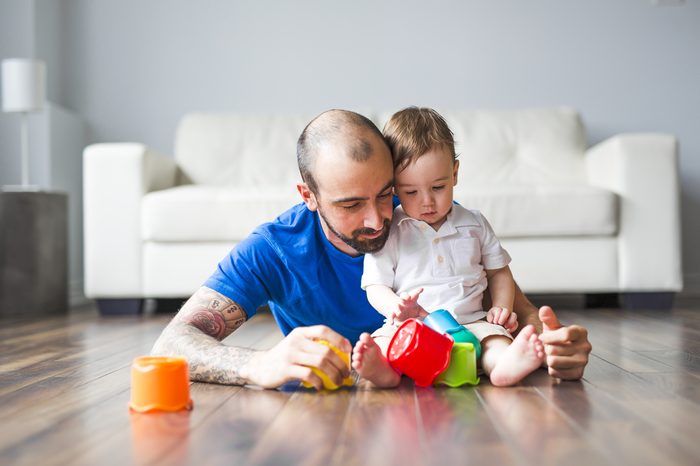 A family, childhood, creativity, activity and people concept - happy father and little son playing with toy blocks at home