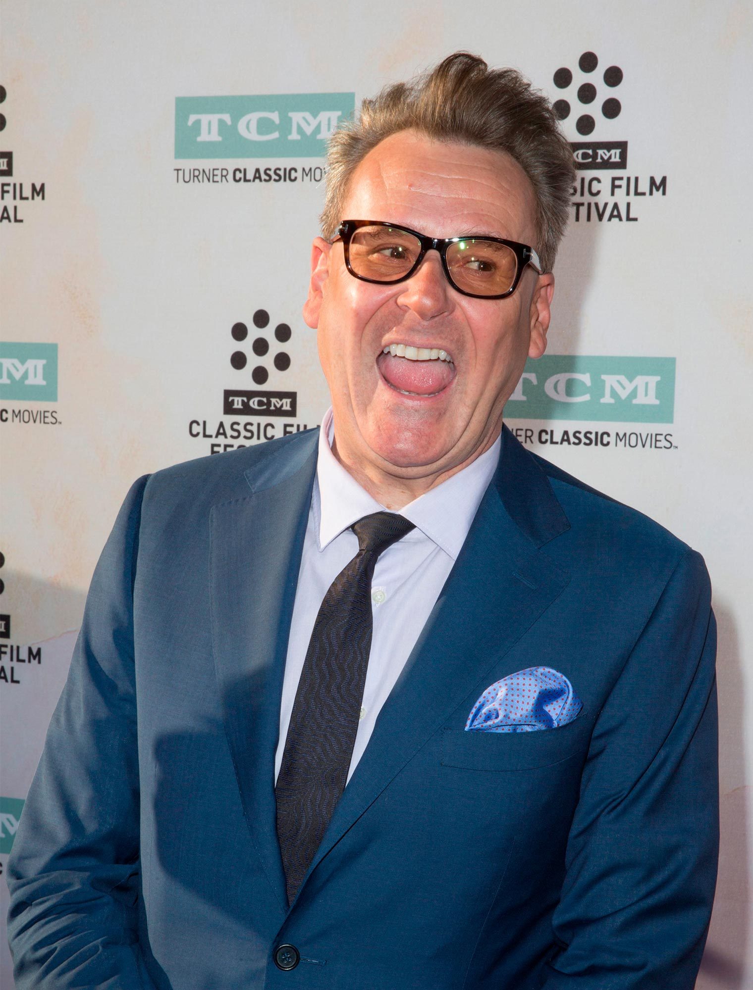 Man in blue suit, smiling widely with tongue out, stands in front of a Turner Classic Movies backdrop.