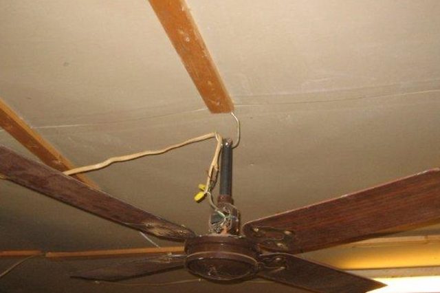 Ceiling fan hangs from wires, appearing unstable, in a wooden-paneled room.