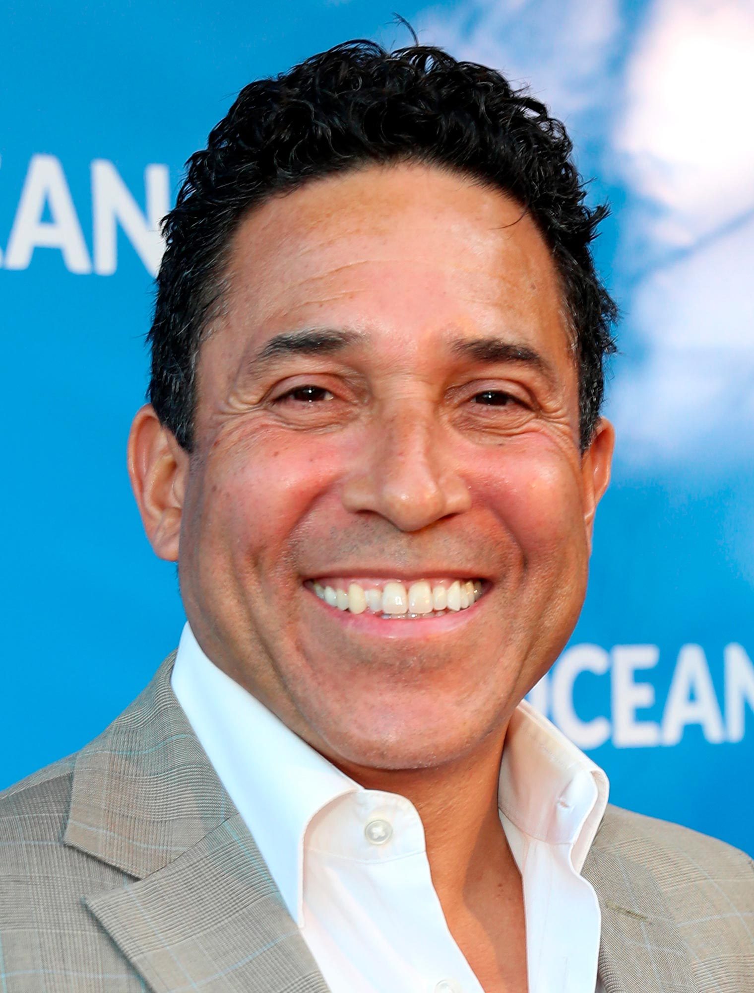 Smiling man wearing a light plaid suit against a blue background.