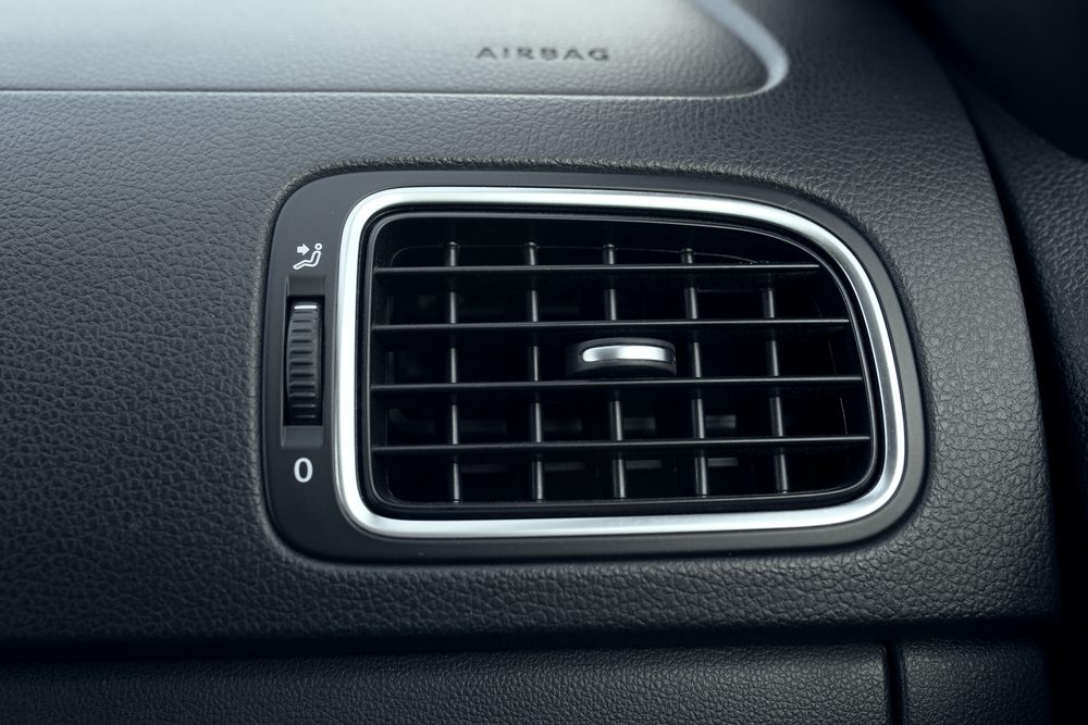 Air vent with adjustable grid sits on a textured dashboard. Text above reads "AIRBAG."