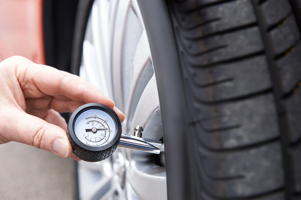 A hand uses a pressure gauge on a car tire in an outdoor setting.