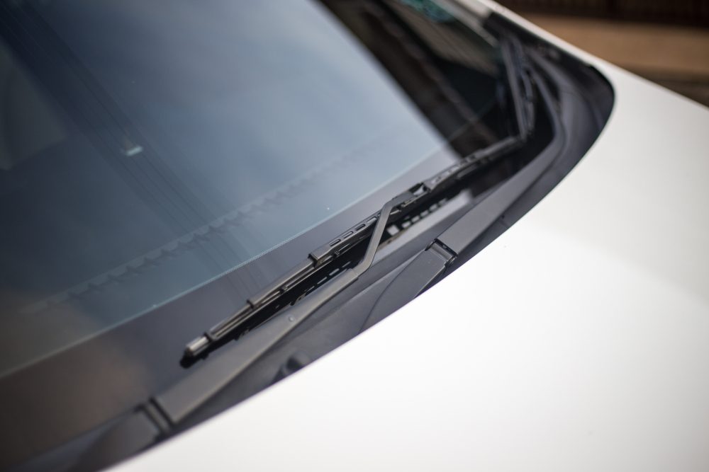 Windshield wipers rest on a car's front windshield, positioned on a clean, white vehicle surface in an outdoor setting.