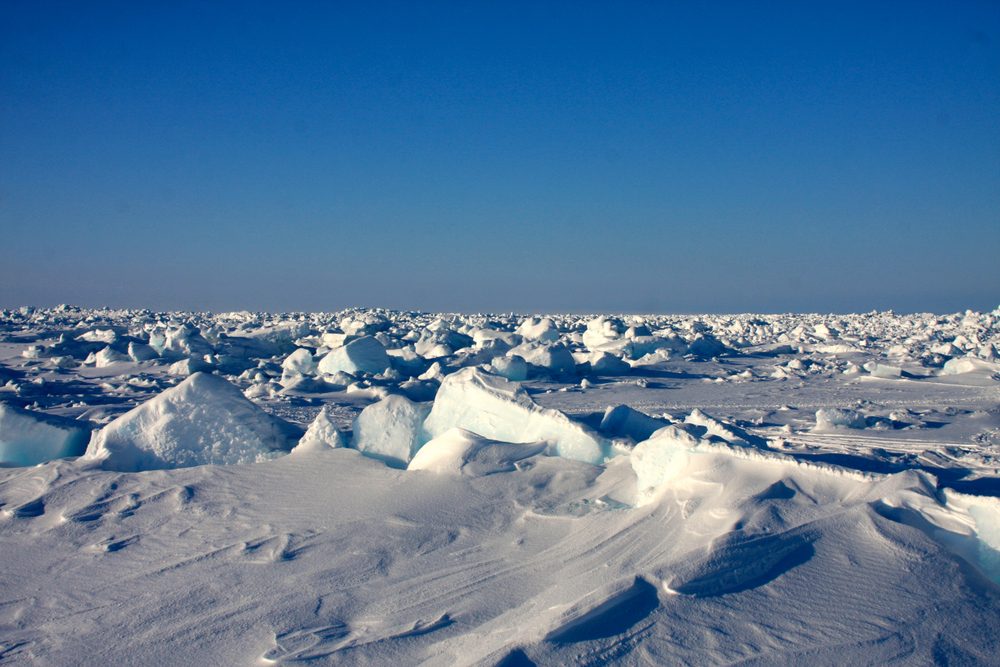 Ice chunks scatter across a vast, snowy landscape under a clear blue sky, creating a serene, frozen panorama.