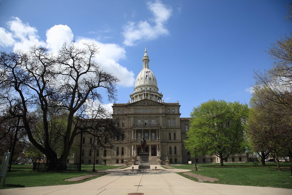 A large, domed building stands prominently under a blue sky, surrounded by leafless and green trees within a park setting.