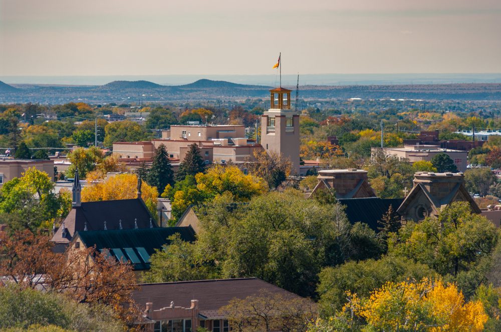 Clock tower stands prominent, surrounded by lush trees, against a backdrop of distant mountains under a clear sky.