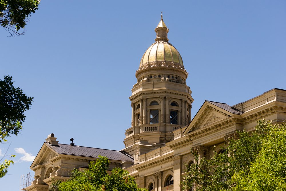Golden-domed building stands majestically amid lush green trees under a clear blue sky, showcasing classical architecture with columns and intricate details.