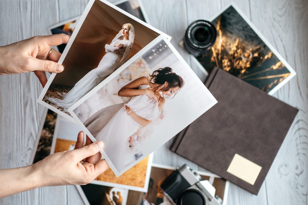 Printed wedding photos with the bride and groom, a vintage black camera, photoalbum and woman hands with two photos