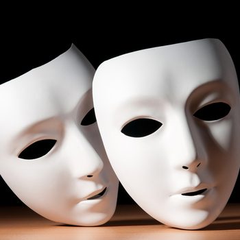 Two white masks rest on each other on a wooden surface, set against a dark background.