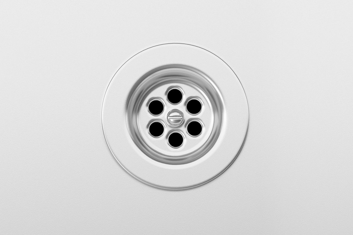 A circular metal drain with six holes, set in a smooth white surface.
