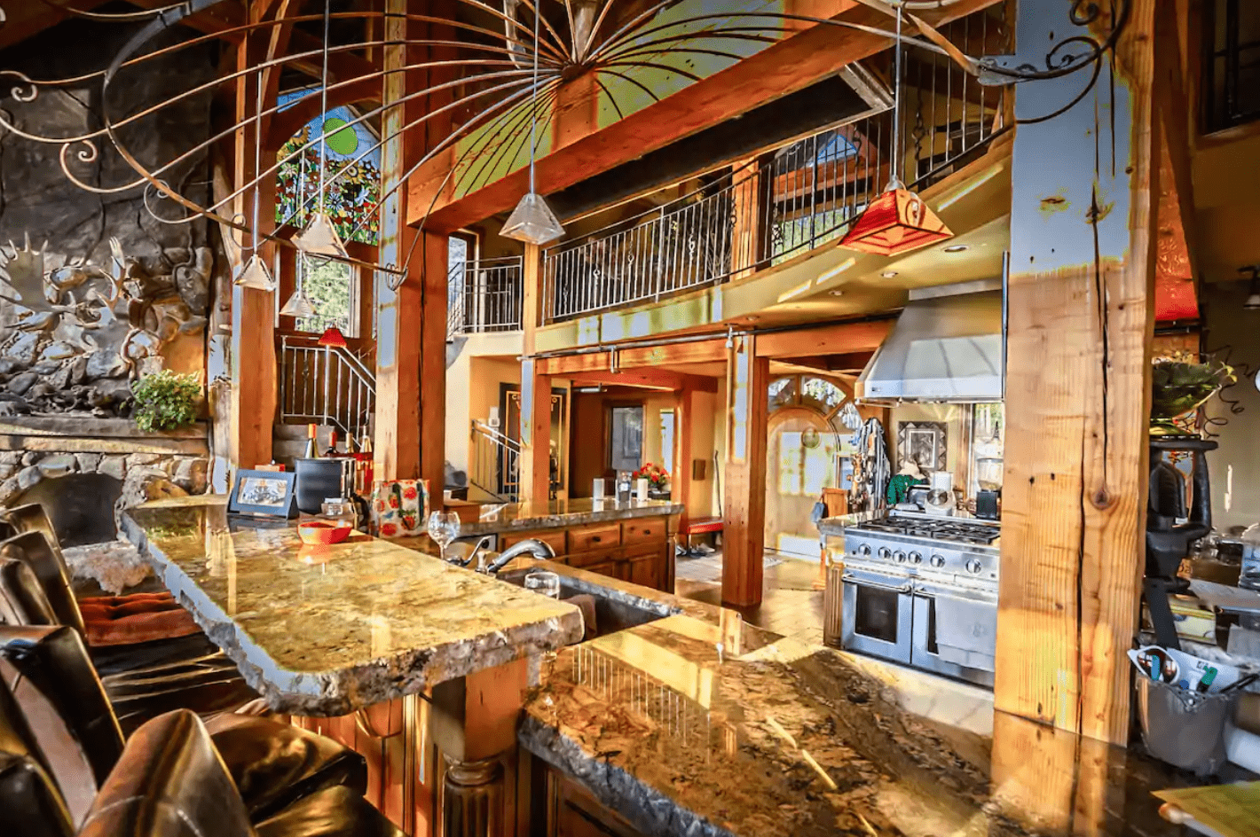 Granite countertop reflects light in a rustic, spacious kitchen with wooden beams, decorative stained glass, and metal chandelier under a high, wood-paneled ceiling.
