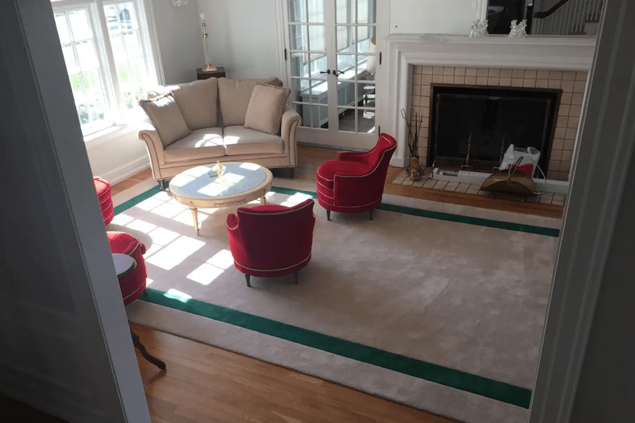 Sofa and chairs surround a coffee table in a sunlit living room with a fireplace, large window, and glass doors.