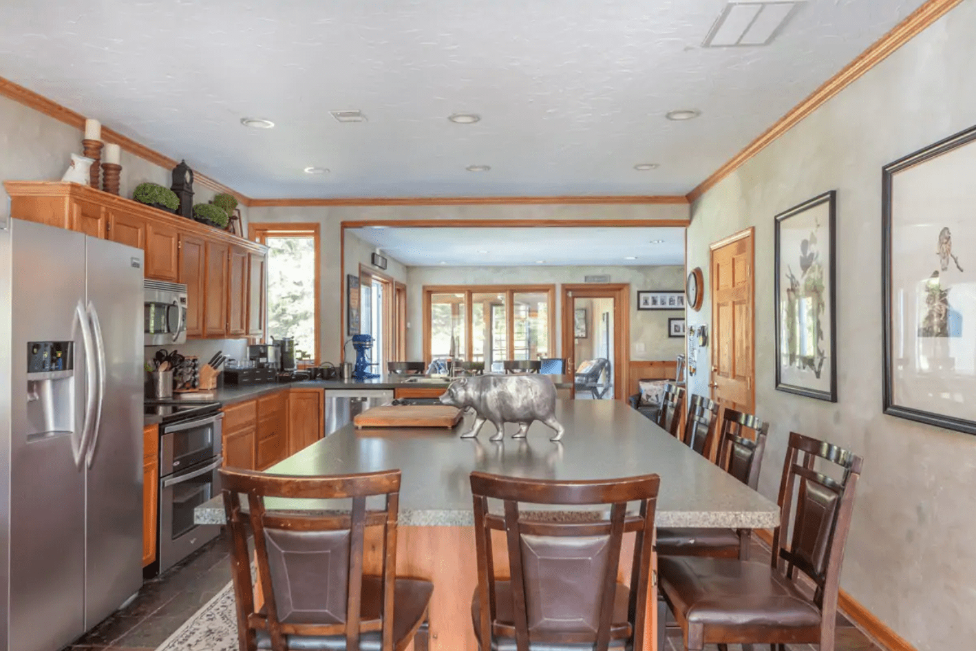 Kitchen island with chair seating, displaying metal animal sculpture, surrounded by stainless steel appliances, wooden cabinetry, and decorative wall art in home setting.