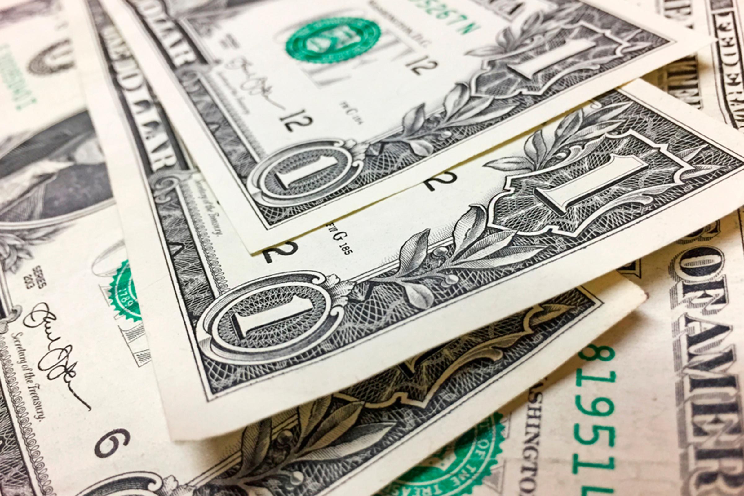 Dollar bills overlapping, showing intricate designs, numerals, and partial text. They are placed on a flat surface, creating a scattered layout.