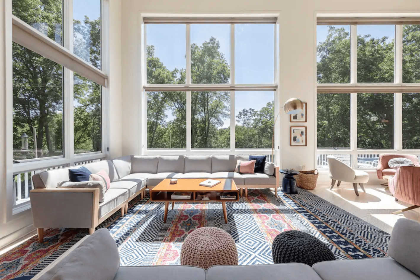 Spacious living room features a large L-shaped sofa facing a wooden coffee table, with large windows overlooking lush greenery and patterned rugs on the floor.