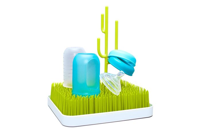 Green grass-like drying rack holds bottles and pacifier, with a cactus-shaped holder, on a white surface.