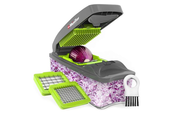 Chopper slices purple onion; features open lid and sharp grid. Context: green blade accessories, full container of diced onions, cleaning tool nearby.