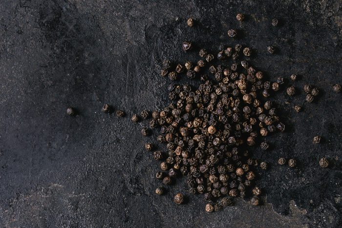 Heap of black pepper peppercorns over old black iron texture background. Top view, copy space. Square image