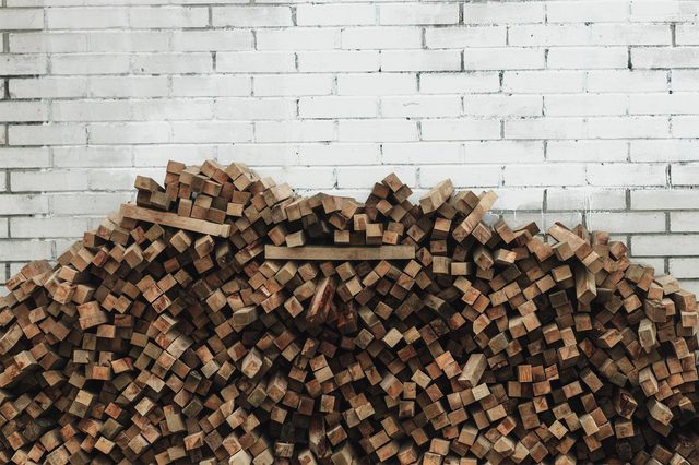 Wooden blocks are stacked against a white brick wall, forming a chaotic pile.
