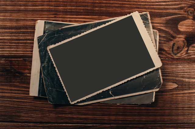 Vintage photos lie scattered, slightly overlapping, against a wooden table backdrop. The images have aged edges, suggesting a collection of old memories.