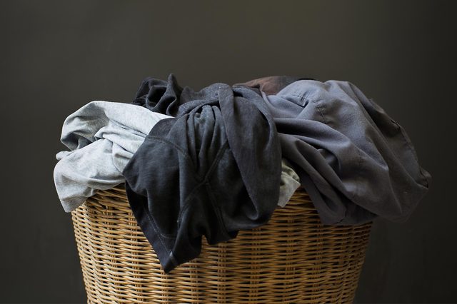 Basket holds a pile of clothes, overflowing, against a plain dark background.
