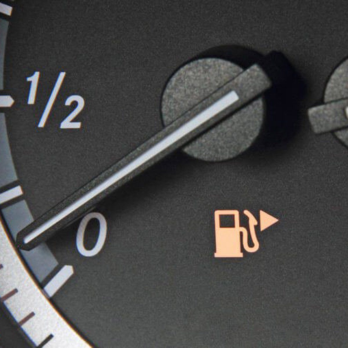 Fuel gauge needle points to empty, indicating low fuel, with a fuel pump icon illuminated in a car dashboard.