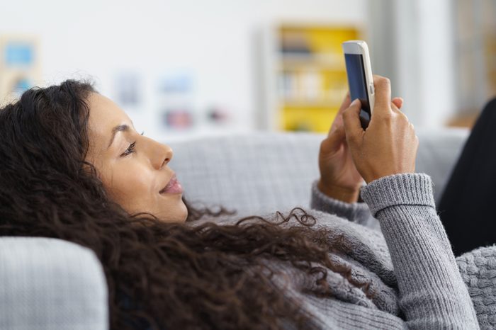 woman lying on the sofa while writing a text message on her cell phone