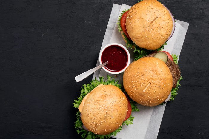 Two hamburger, cheeseburger and sauce on dark surface with copy space, top view