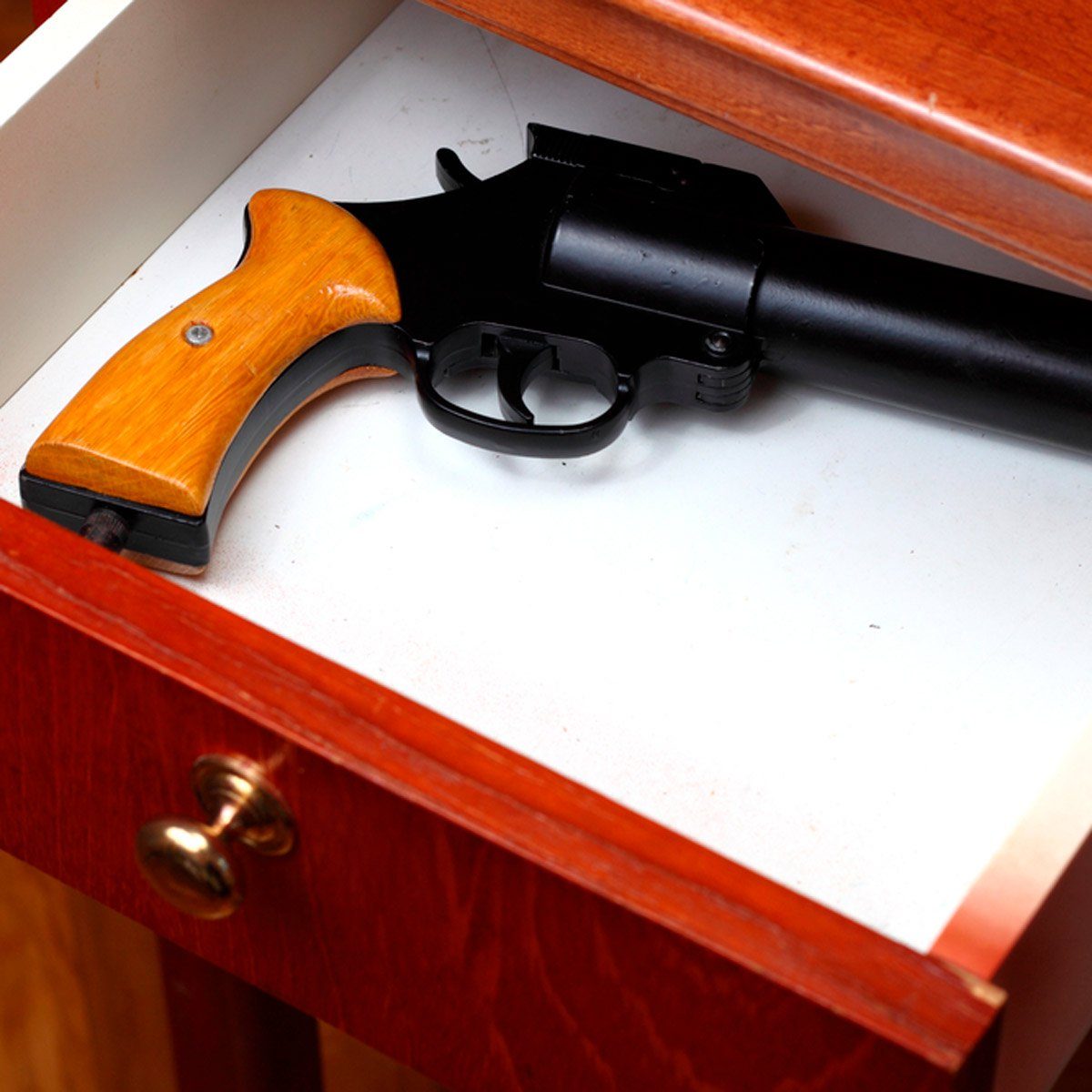 A revolver lies inside an open wooden drawer, resting securely on a white surface.