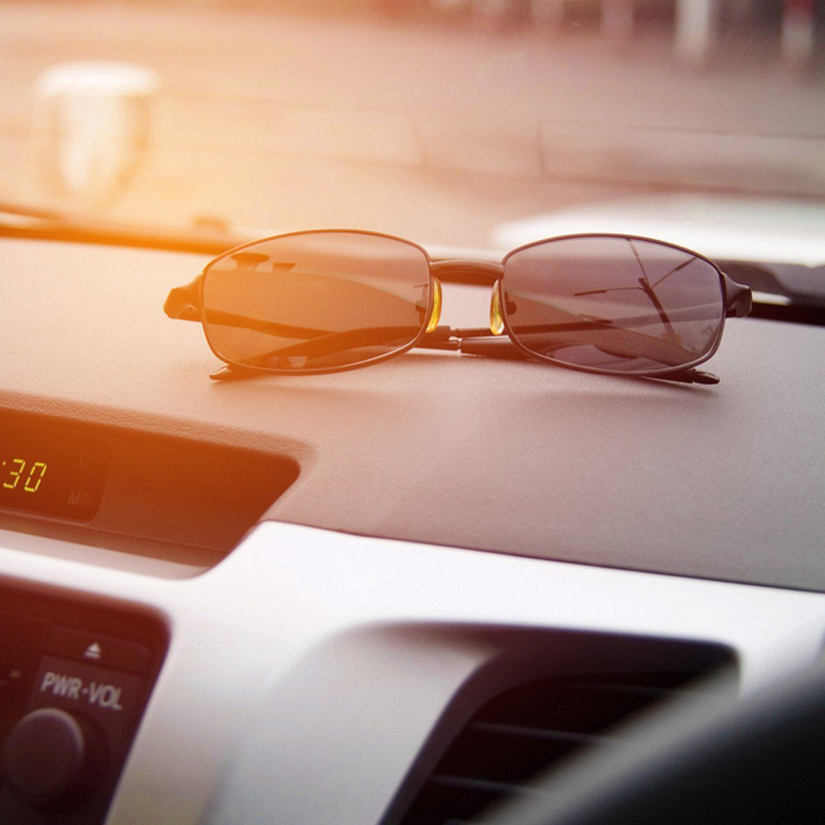 Sunglasses resting on a car dashboard, with sunlight streaming through the windshield, illuminating the car's interior.