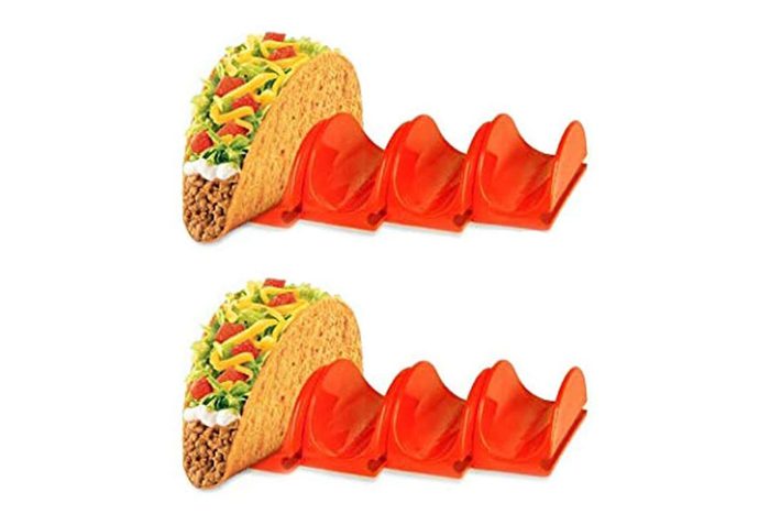 Tacos rest in orange plastic holders on a white background, showcasing their toppings of lettuce, cheese, tomatoes, and ground meat.