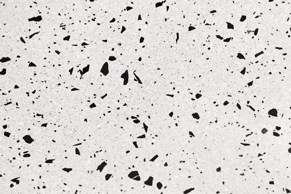 Speckled black fragments scattered across a light gray, textured surface.