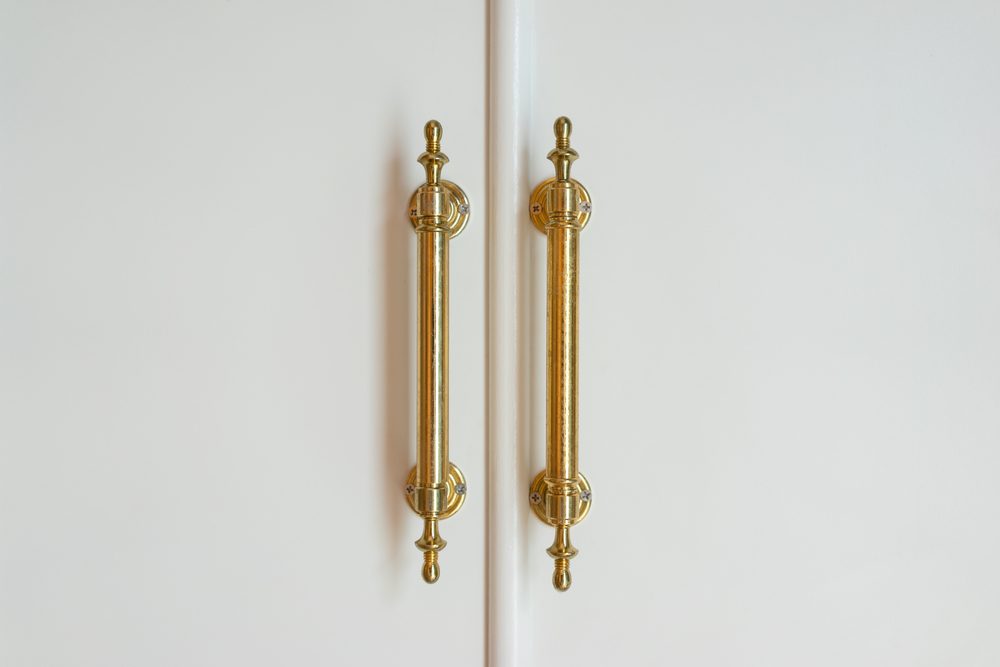 Two ornate, vertical gold handles adorn a white double door.