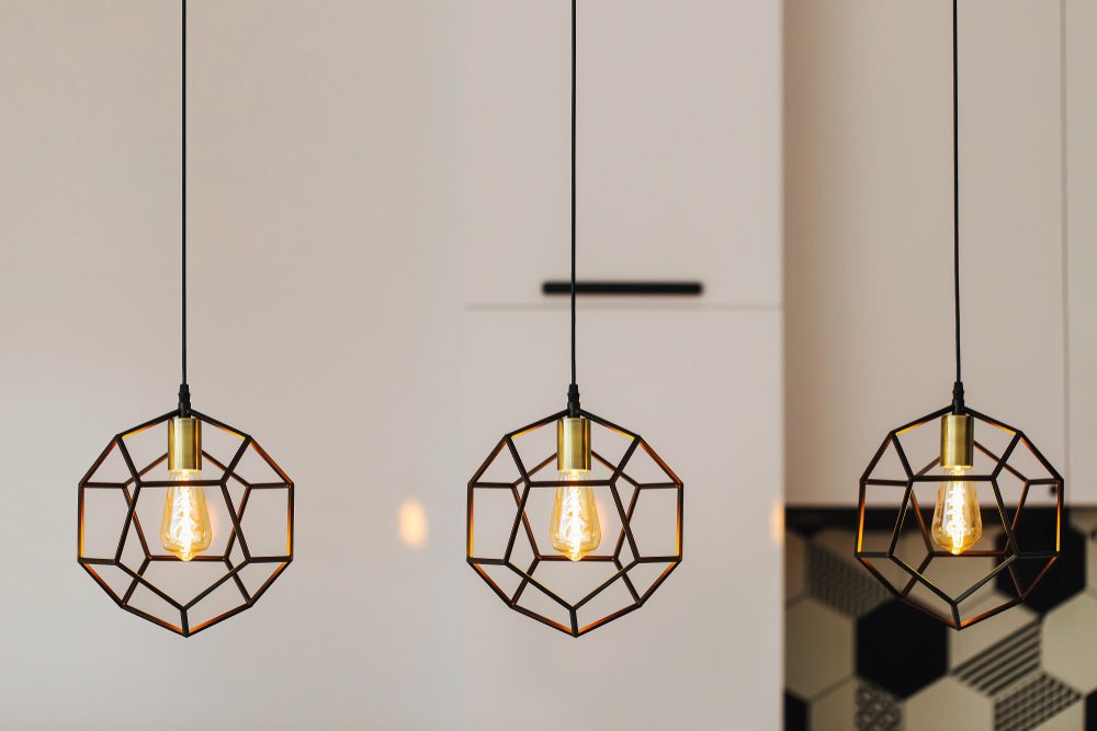 Three geometric pendant lights hang in a modern kitchen, illuminating the space warmly.
