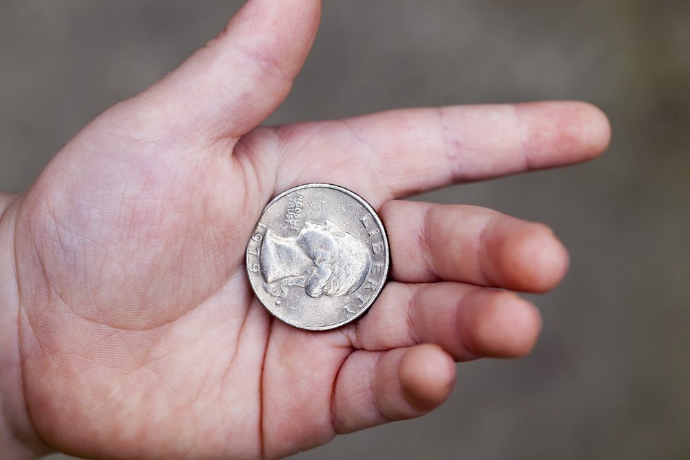 A silver coin lies in an open palm against a blurred gray background.