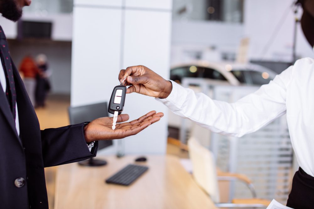 Young car african female salesman giving a key from the new car to the beautiful young african couple owners