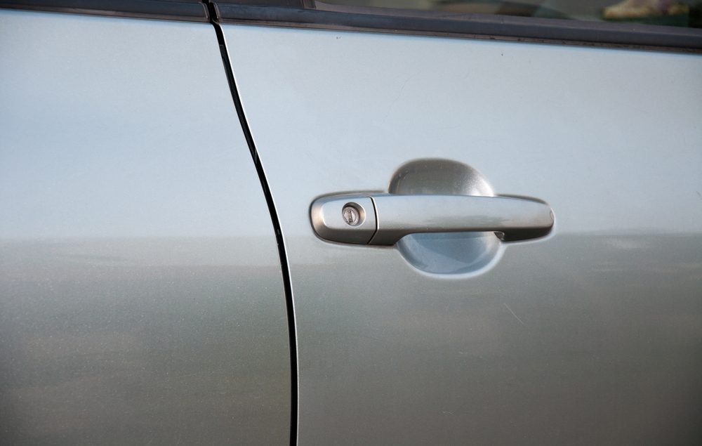 Car door handle, resting, on a silver vehicle's side, with a visible keyhole, surrounded by metallic paint reflecting light.