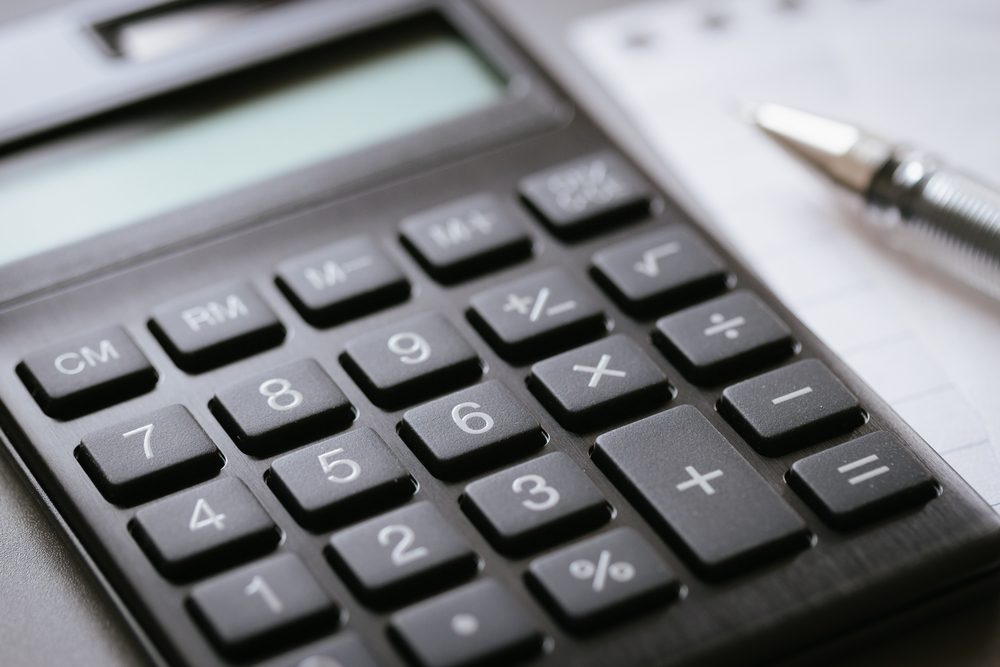 Calculator resting beside a metallic pen and paper, on a desk, with buttons visible including numbers, arithmetic symbols, and "CM" key.