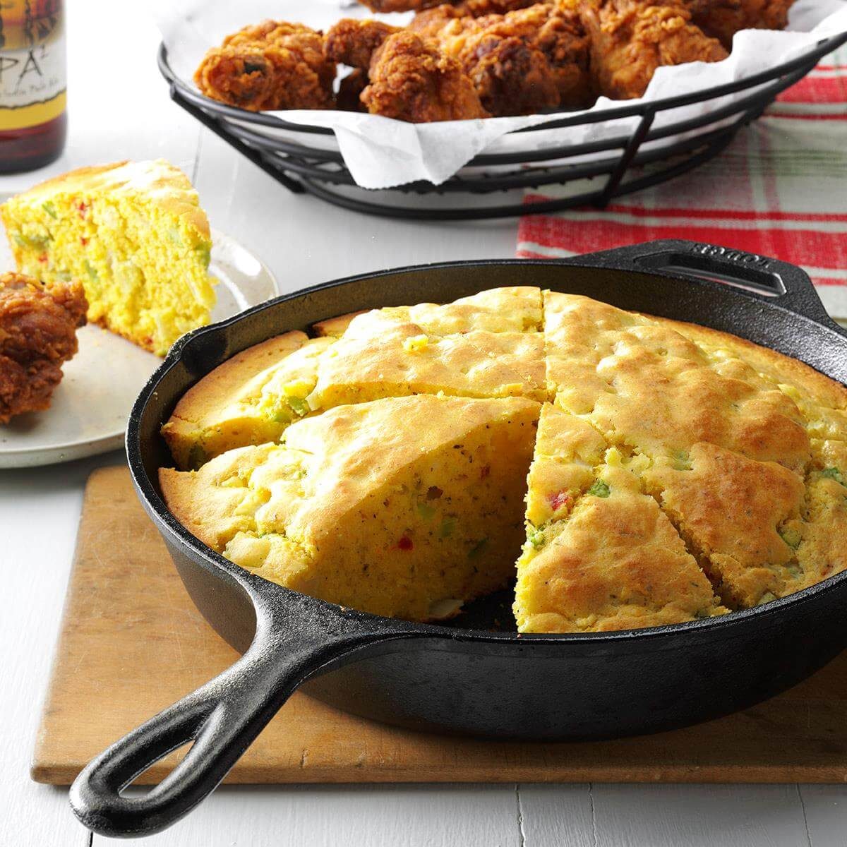 Cornbread sits sliced in a cast iron skillet beside a plate, with fried chicken visible in the background.