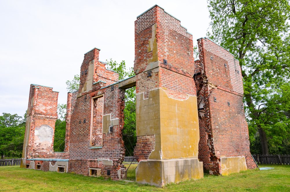 Brick ruins stand tall, showing weathered openings amid lush green grass and trees in a peaceful, overcast outdoor setting.