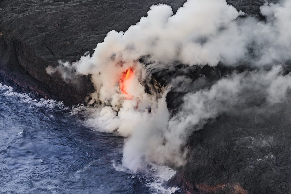 Molten lava pours into the ocean, creating billowing steam among rugged black cliffs.