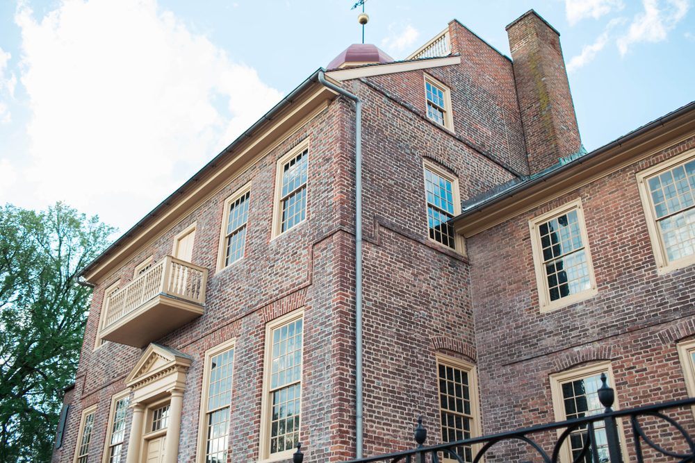 Brick building stands tall against a blue sky, featuring numerous windows and a small balcony. Nearby, a tree provides natural contrast.