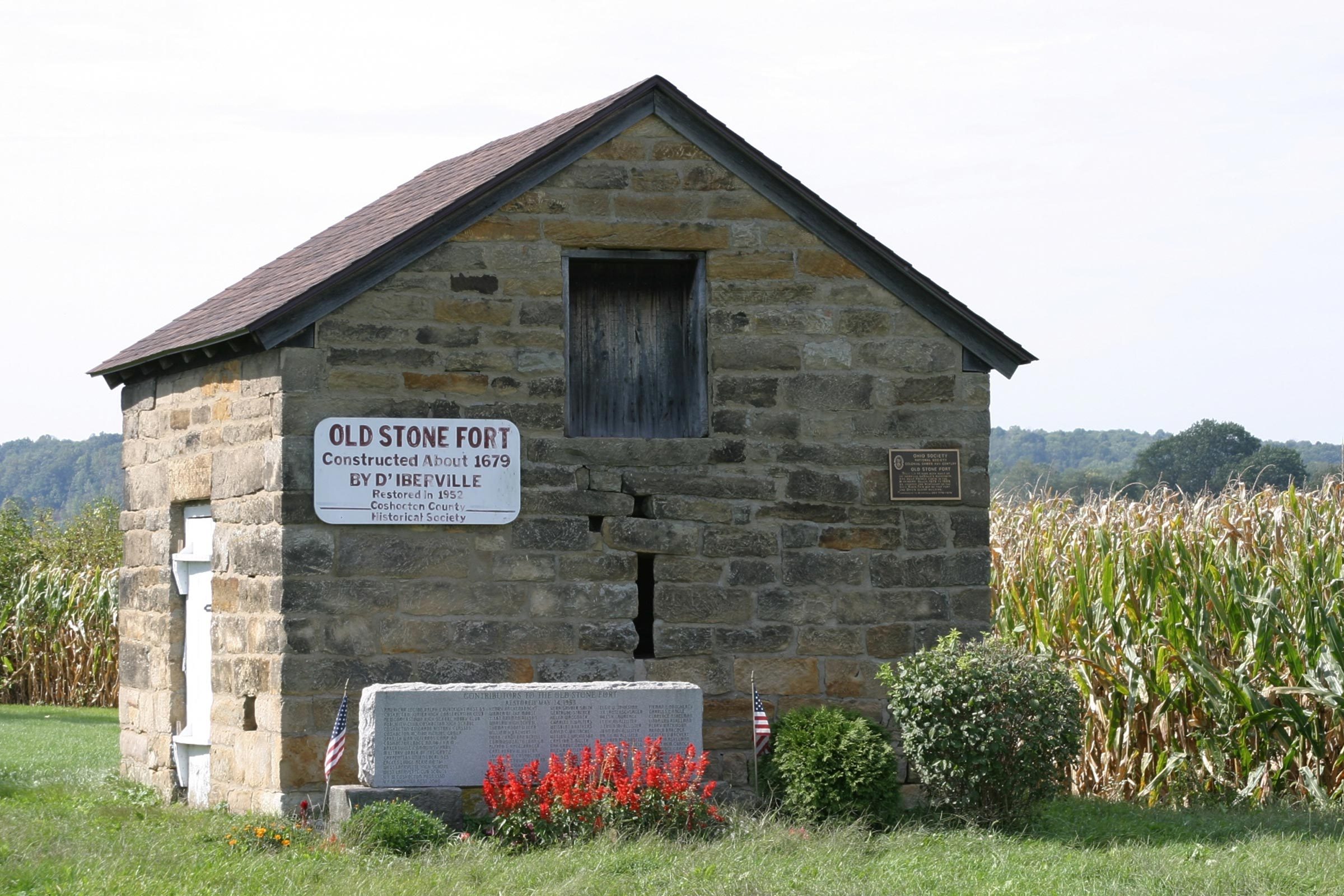 Stone fort stands amidst a grassy field with nearby cornfield; sign reads, â€œOld Stone Fort, Constructed About 1679 by Dâ€™Iberville, Restored in 1952.â€