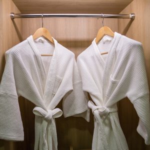 Two white bathrobes hang on wooden hangers inside a wooden wardrobe.