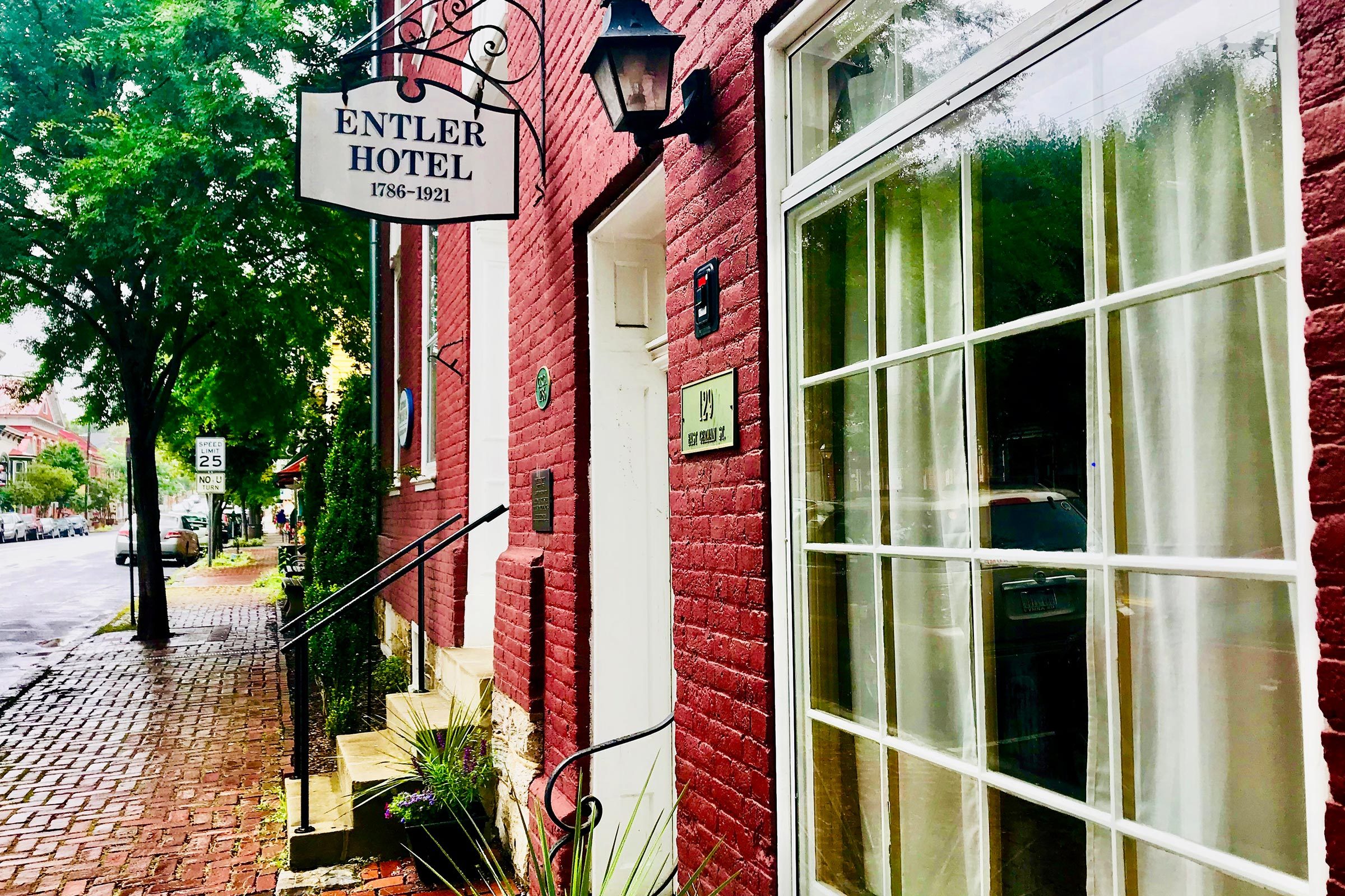 A sign for "Entler Hotel 1786-1921" hangs above a red brick building entrance, with a tree-lined street and speed limit sign nearby.