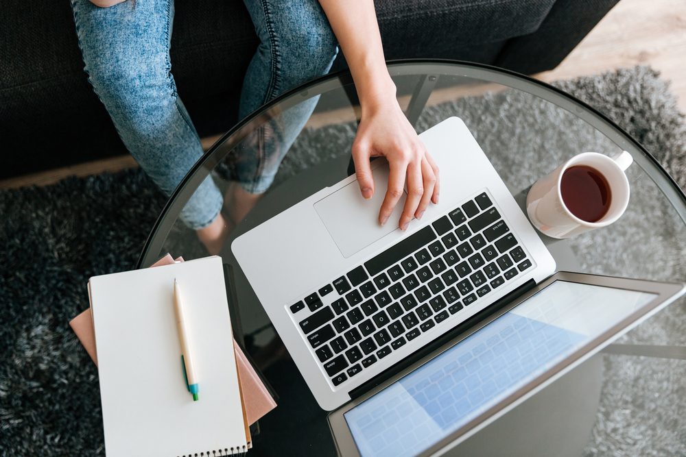 Closeup of woman sitting and using laptop on glass table at home