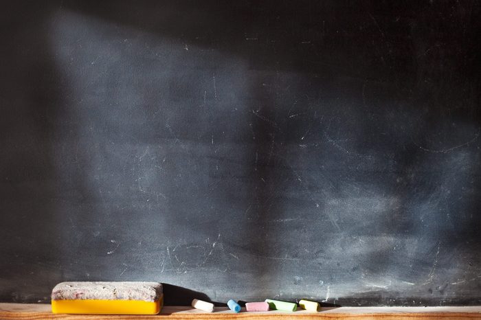 Blank blackboard with colored chalks and eraser and light effect. Horizontal composition.