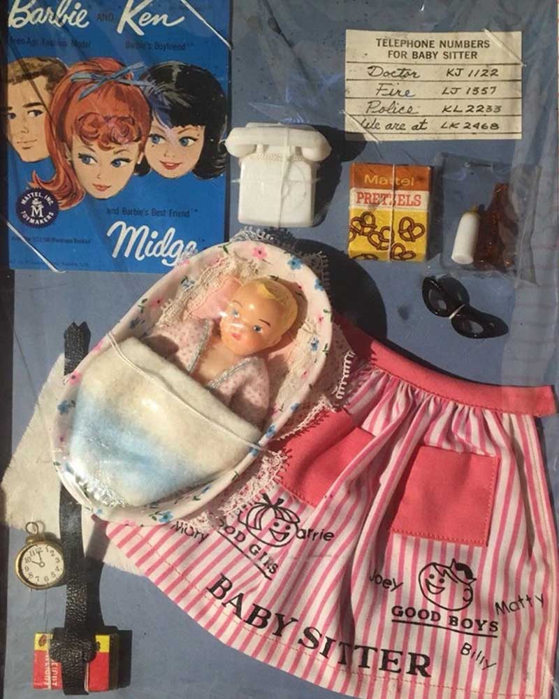 Baby doll lies in a basket with a babysitter's apron nearby. A phone, pretzel box, and glasses complete the vintage doll set.