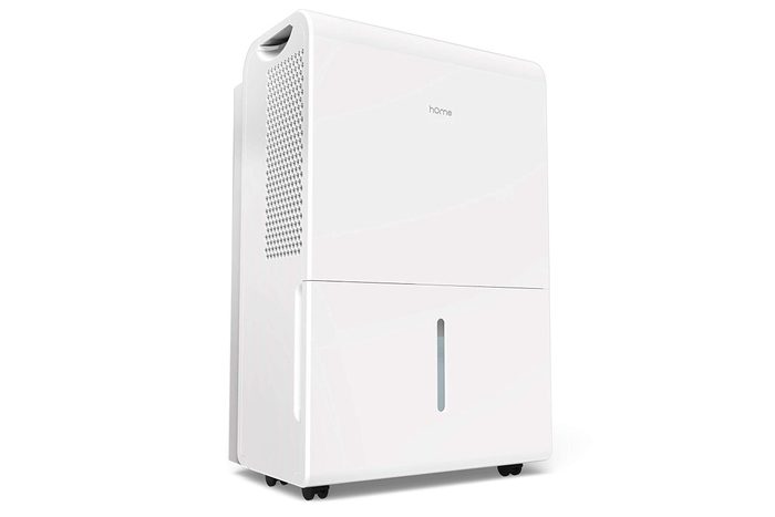 A white dehumidifier stands upright, featuring a grated side panel and a water level window at the bottom, set on small wheels.