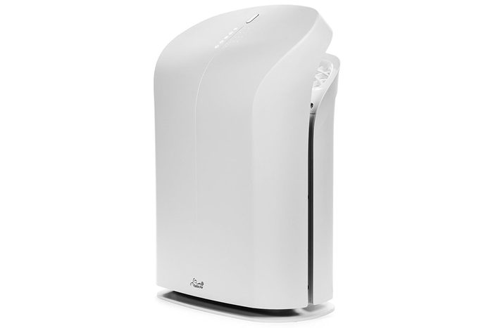 White air purifier stands upright; curved design; minimalistic backdrop; small control panel on top; front logo; vent partially visible on side.